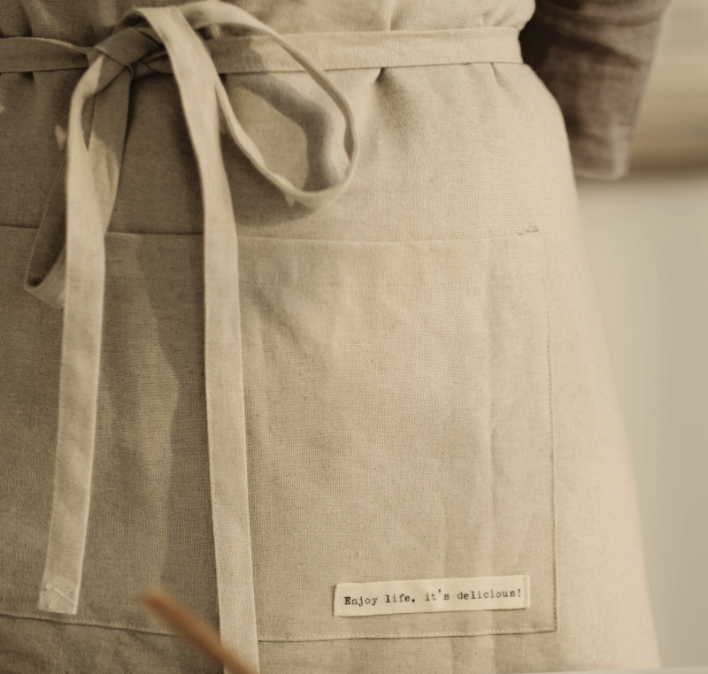 A linen apron with a label reading Enjoy life, it&rsquo;s delicious